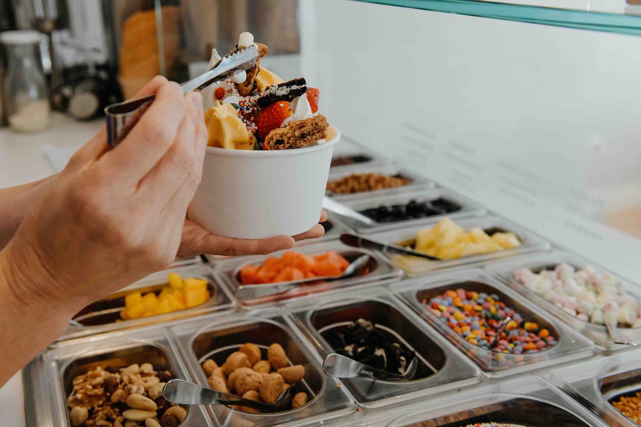 Hand füllt einen Frozen-Joghurt-Becher an der Topping-Bar